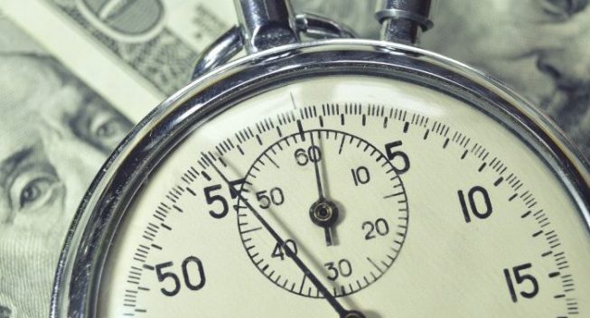 stopwatch lays over US dollar banknotes; focus on watch arrow